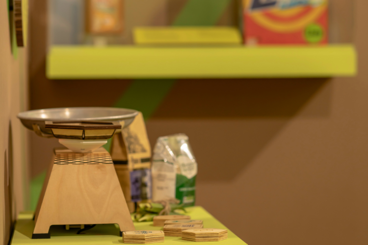 Scales and some weights in the foreground, with a bag of rice and other objects in the background.