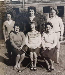 Black and white image of people, some seated and some standing. The front row of people are holding golf clubs.