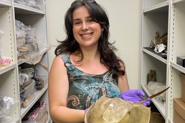 A female student wearing gloves and smiling at the camera and holding up a specimen.